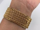 a woman ' s hand holding a gold bracelet on a white plate