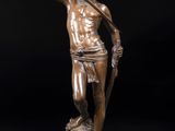 une statue en bronze représentant un homme tenant une lance, sur fond noir