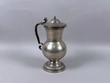 une cafetière ancienne en métal argenté, munie d'une anse, sur fond blanc