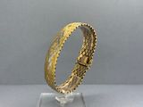 a close up of a gold bracelet on a clear surface