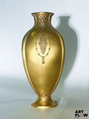 a gold vase that is sitting on a white surface