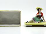 a figurine of a woman sitting on a bench next to a box