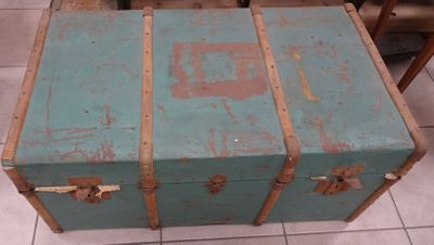 une malle bleue posée sur un sol carrelé, à côté d'une chaise
