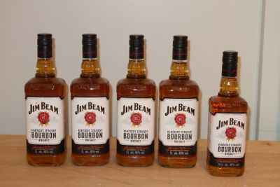 Quatre bouteilles de bourbon sont posées sur une table devant un mur blanc.