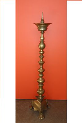 two different views of a tall brass candle stand against a red wall