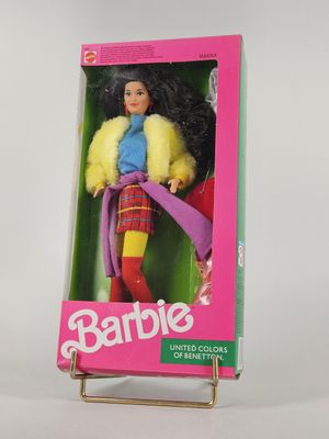 une poupée Barbie dans une boîte, posée sur une surface blanche avec un fond rose