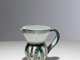 une cruche verte et blanche posée sur une table blanche, sur fond gris