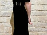 a woman standing in front of a stone wall wearing a black dress