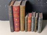 Plusieurs vieux livres sont alignés sur une étagère devant un tableau noir.