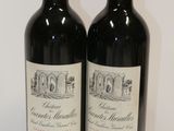 two bottles of red wine sitting on top of a white table