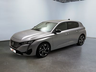 La voiture argentée est garée dans une grande pièce aux murs blancs.