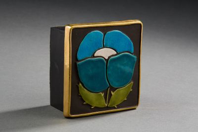 une fleur bleue et verte sur une boîte noire et dorée posée sur une surface grise