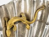 a gold lizard on a silver shell on a white background