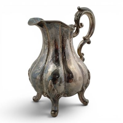 an old silver pitcher sitting on a stand on a white surface