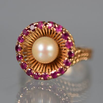 Gros plan sur une bague ornée d'une perle et d'un rubis, posée sur une surface réfléchissante