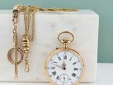 une montre de poche en or et une chaîne en or posées sur un bloc de marbre
