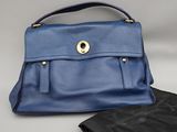 un sac à main en cuir bleu et un pantalon en cuir noir posés sur une table
