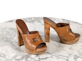 des mules en cuir de style « clogger » à talon en bois et boucles, posées sur une table en marbre