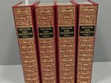 trois livres rouges et dorés posés sur une table blanche