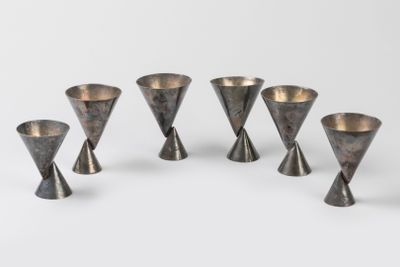 six vases en argent sont disposés en cercle sur une surface blanche