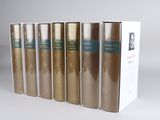 six books are lined up in a row in front of a white box