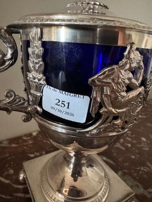 un trophée en argent posé sur une table, à côté d'un verre bleu