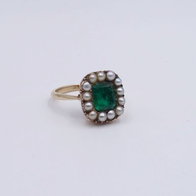 a close up of a ring with a green stone and pearls