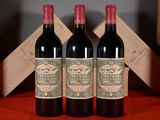 trois bouteilles de vin rouge posées sur une table, à côté d'une caisse en bois