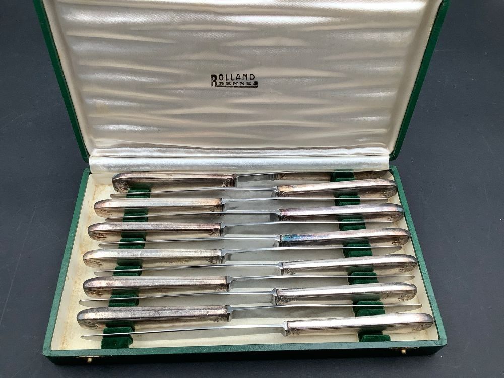 Lot de 12 couteaux, lames inox crantées et manches en métal argenté. Etat d’usage, présentés dans un écrin.