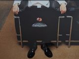 une photo d'un homme assis sur une chaise, une pomme sur les genoux