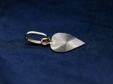 a close up of a silver leaf charm on a blue cloth