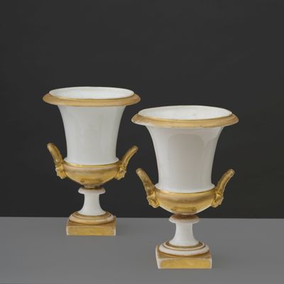 deux vases blancs et dorés munis d'anses, posés sur une table