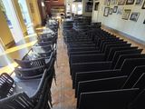 des rangées de chaises noires dans une pièce où sont accrochés des tableaux aux murs