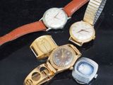 Plusieurs montres sont posées sur une surface noire, avec un bracelet doré.