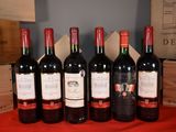 six bottles of red wine are lined up on a table