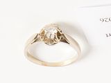 un gros plan d'une bague sertie d'un diamant, posée sur une surface blanche