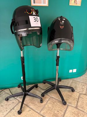 pair of black hair dryers on stands in front of a green wall
