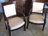 two wooden chairs with beige upholstered cushions sit in front of a dresser