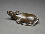 bronze figurine of a bull lying down on a gray surface