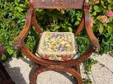 a wooden chair with a cushion on it in front of a bush