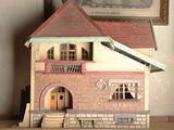 une petite maison de poupées posée sur une étagère, à côté d'une photo encadrée