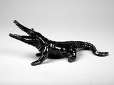 figurine d'alligator noir assis sur une surface blanche, la gueule ouverte