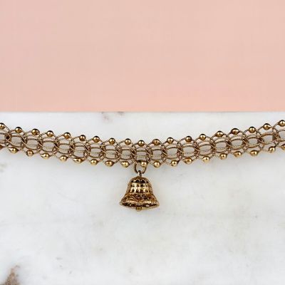 un gros plan sur un bracelet en chaîne dorée orné d'une breloque en forme de clochette