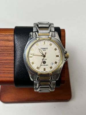 une montre en argent et en or posée sur un socle en bois