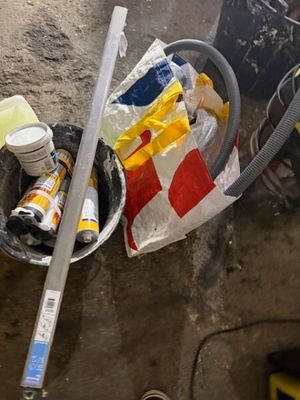 un seau rempli d'objets posé par terre à côté d'un tuyau d'arrosage