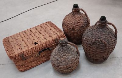 trois bouteilles en osier et un panier en osier posés sur une surface en béton