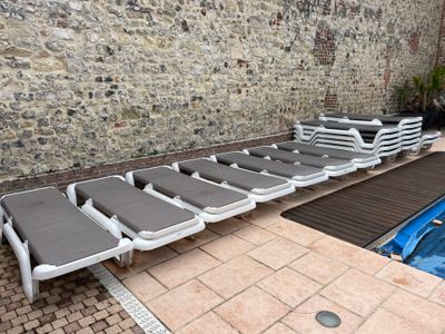 rows of lounge chairs next to a swimming pool in front of a stone wall