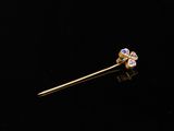 a close up of a gold plated stick pin with a purple flower