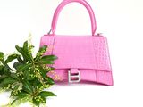 pink crocodile skin handbag next to a green plant on a white surface