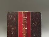 un vieux livre posé sur une table blanche à côté d'un livre rouge